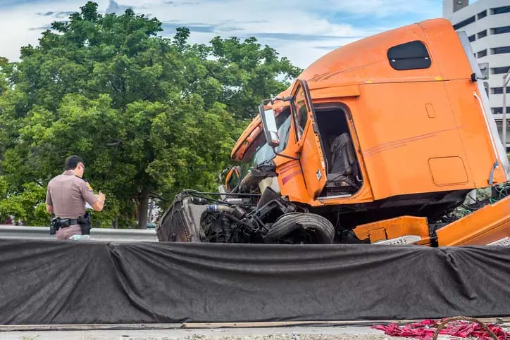 Orange semi-truck with severe front-end damage after a crash, with a law enforcement officer at the scene.